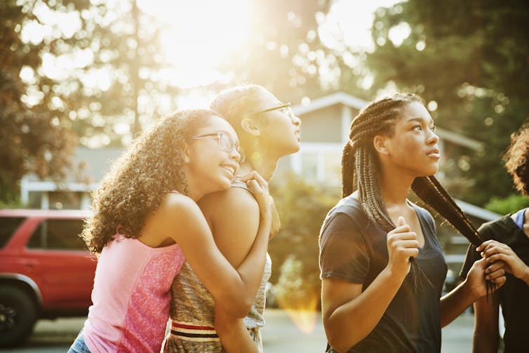 Teenage girl embracing friend while hanging out in neighborhood on summer evening.