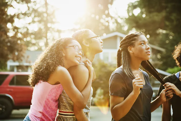 Teenage girl embracing friend while hanging out in neighborhood on summer evening.