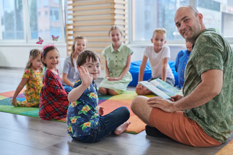 A circle of children sitting on the floor with an adult reading to them