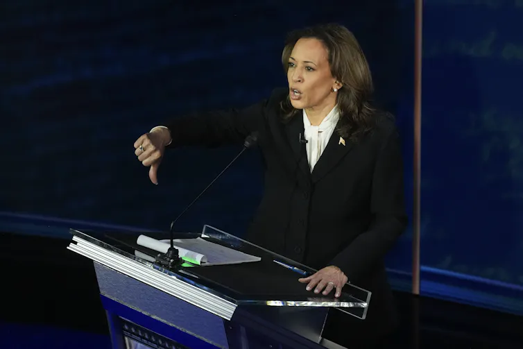 Kamala Harris stands behind a lecturn giving a thumbs down