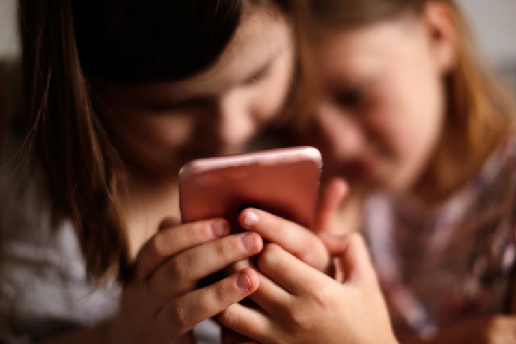 Two young girls look at smartphone together.