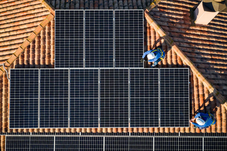 Aerial view of two workers installing solar panels on a rooftop