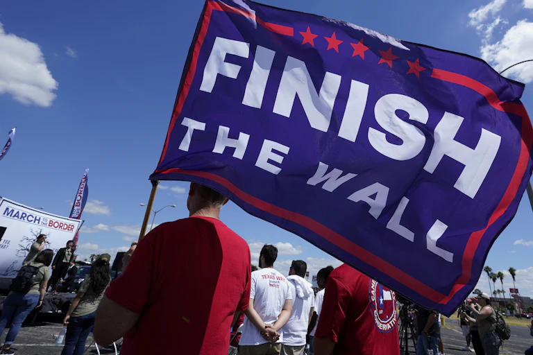 A man carries a blue flag with the words finish the wall
