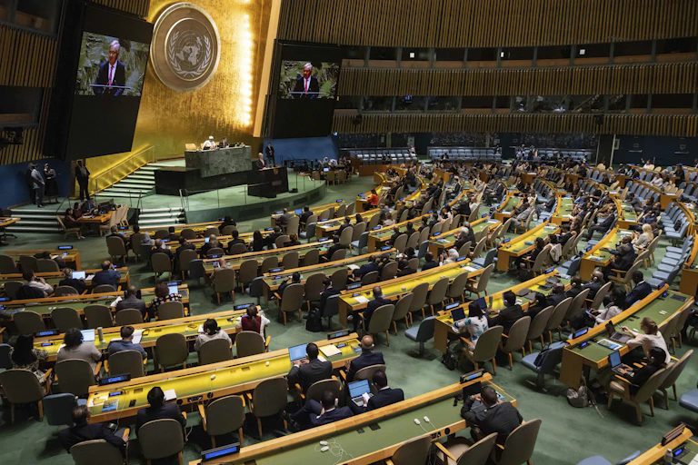 A large auditorium with the UN logo on a gold wall at the front