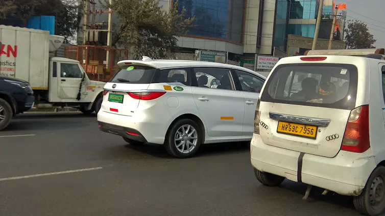 An electric vehicle with green numberplates and a petrol-fuelled vehicle with yellow plates on an Indian road