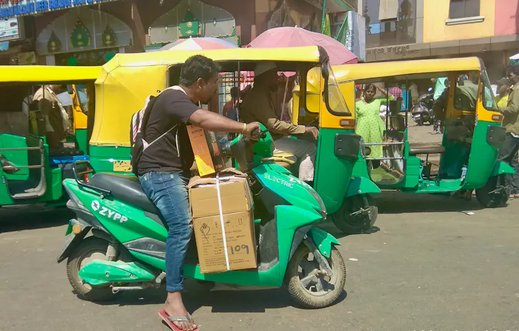 A man transports a large cardboard parcel on an electric motorbike