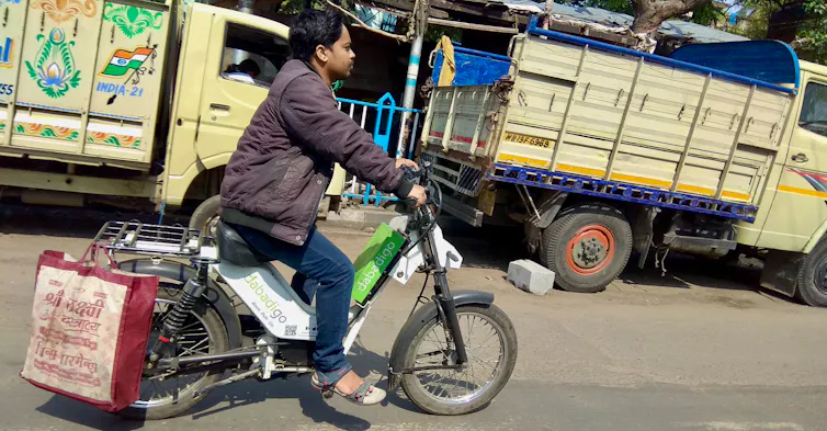 A man rides a hired electric scooter on an Indian street