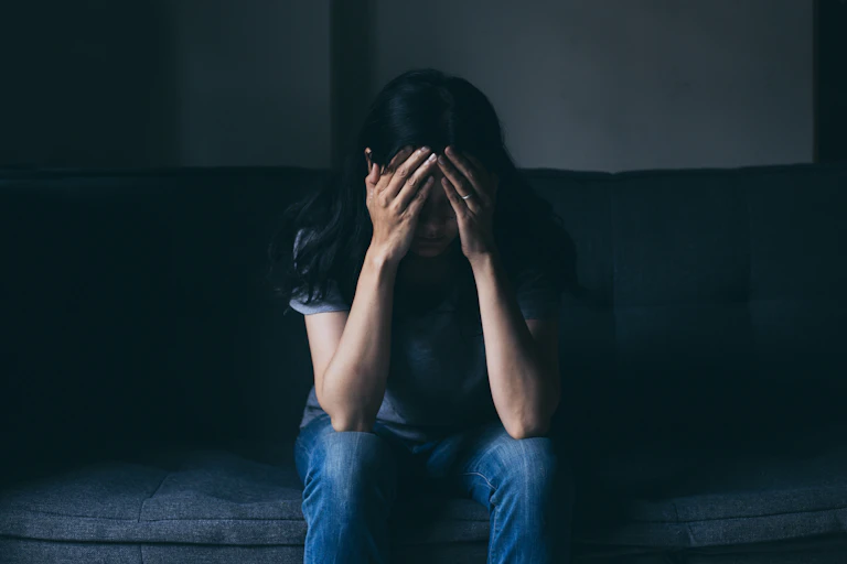 A woman in a dark room puts her hands to her head.