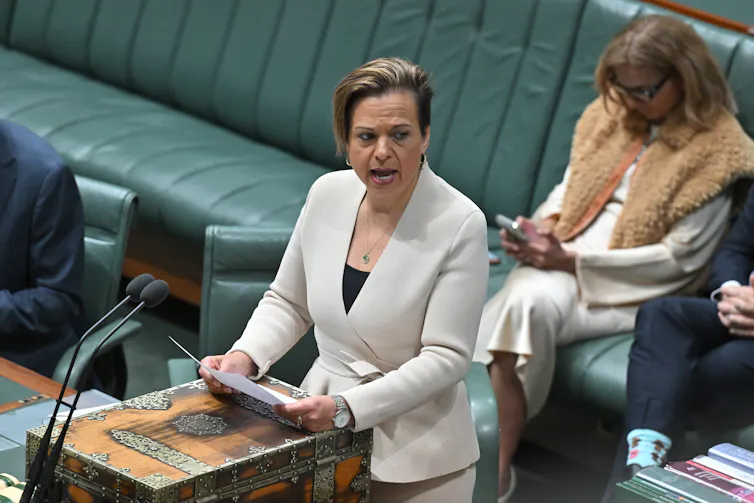 Woman in a white suit speaking at a lectern.