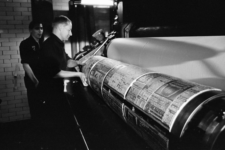 Black and white archive photo of two men standing at a printing press, printing the Sun