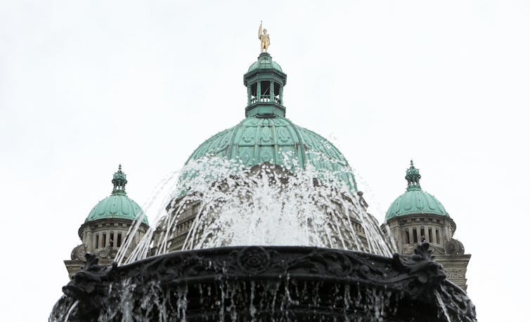 A fountain in front of a legislative dome, with a gold statue of a man at its peak.