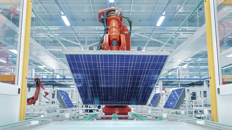 Huge orange robot arm lifts big new blue solar panel in brightly lit factory