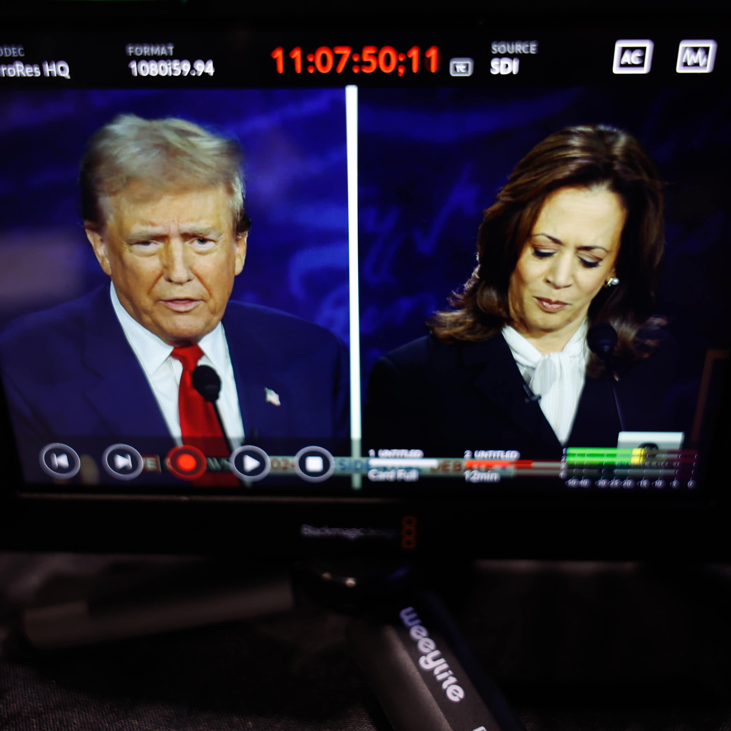 A man with a blue jacket and red tie is seen on a split screen with a woman with dark hair and a dark jacket looking down.