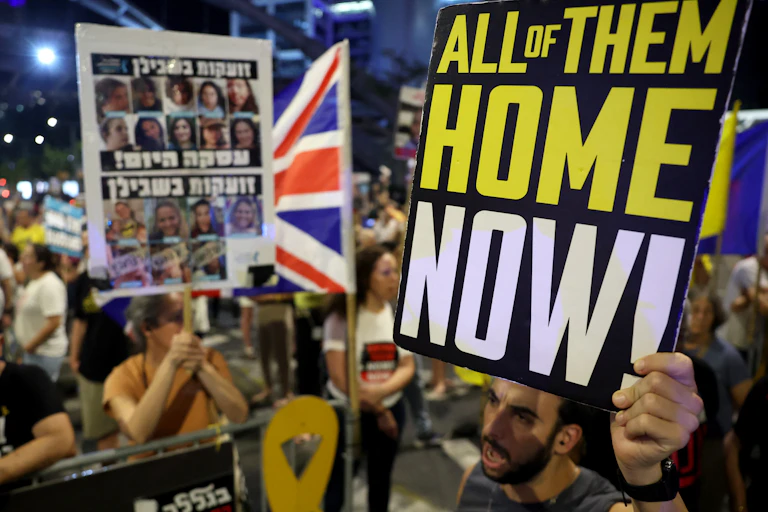 Demonstrators holding signs, one of which says 'ALL OF THEM HOME NOW!'