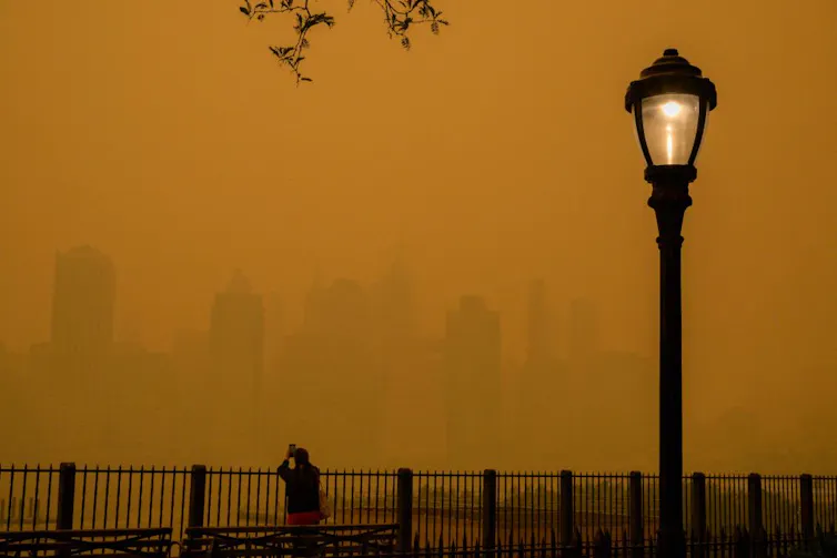 Orange haze blanketing a city skyline, small silhouette of a person taking a photo by a streetlight