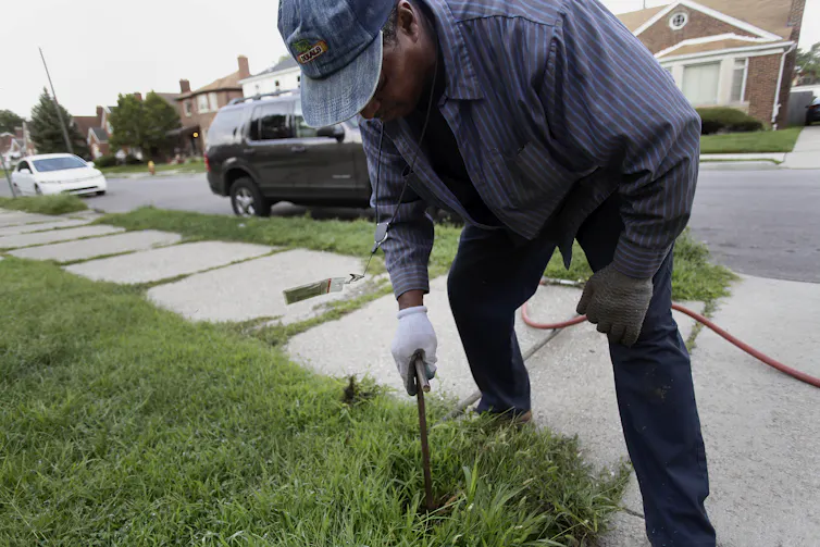 Man outside of home using contraption in the lawn to shut off water to the home