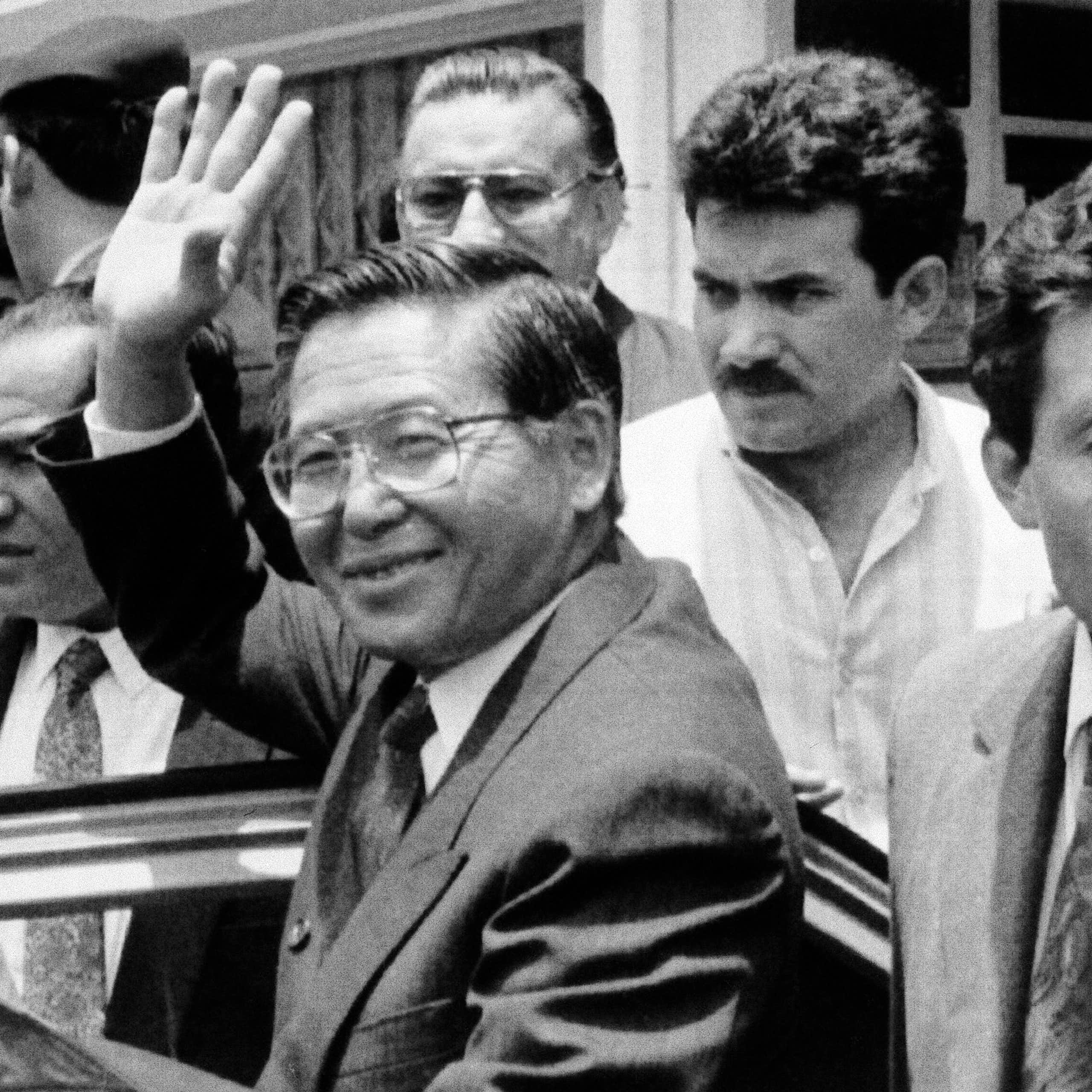 Man in suit smiles and waves in black and white photo.