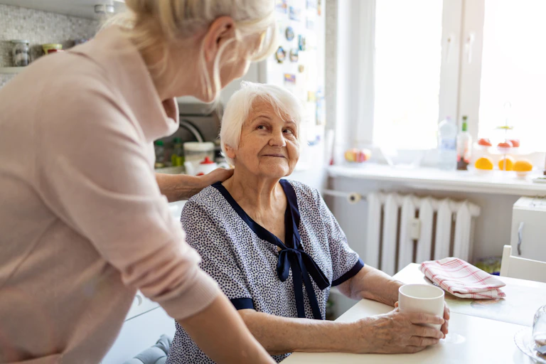 An elderly lady sitting at a kitchen table, talking to a younger lady.