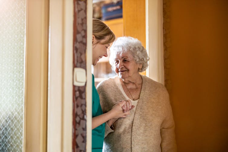 A senior woman with a nurse standing in a doorway.