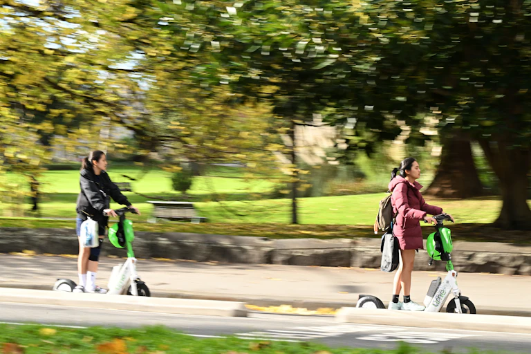 Two people riding e-scooters without helmets in Melbourne