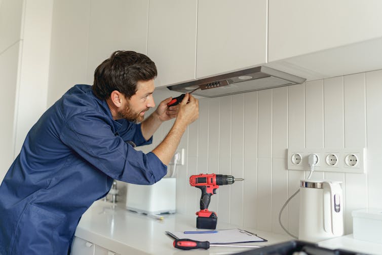 A tradesman fixes an exhaust fan above a stove.