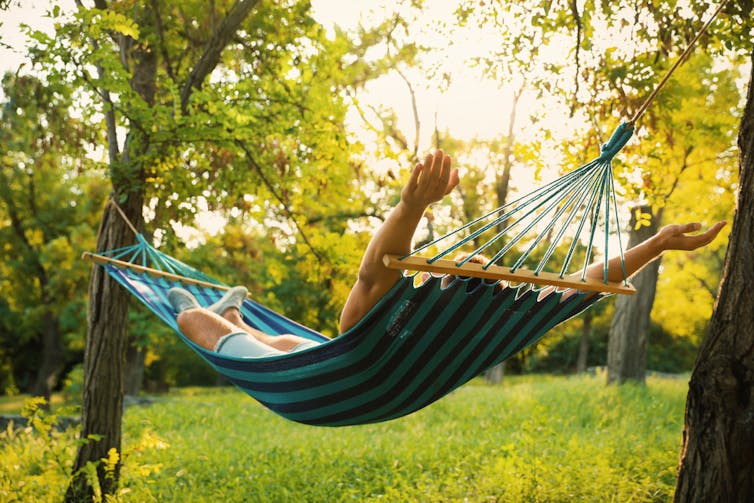 Man in hammock, strung between two trees, arms outstretched