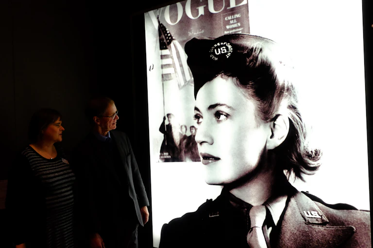 Two people looking at a portrait of Lee Miller in a gallery.