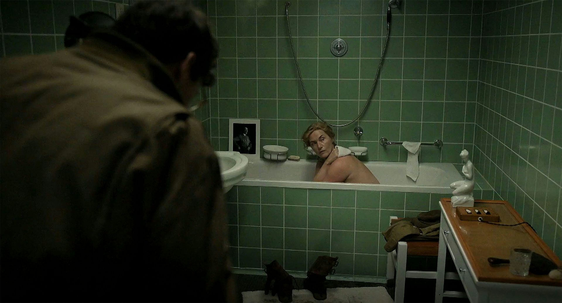A woman sitting in a bath in a green-tiled bathroom