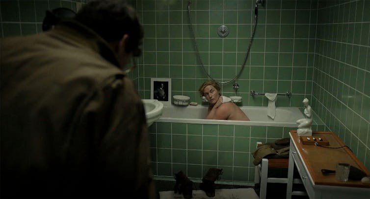 A woman sitting in a bath in a green-tiled bathroom