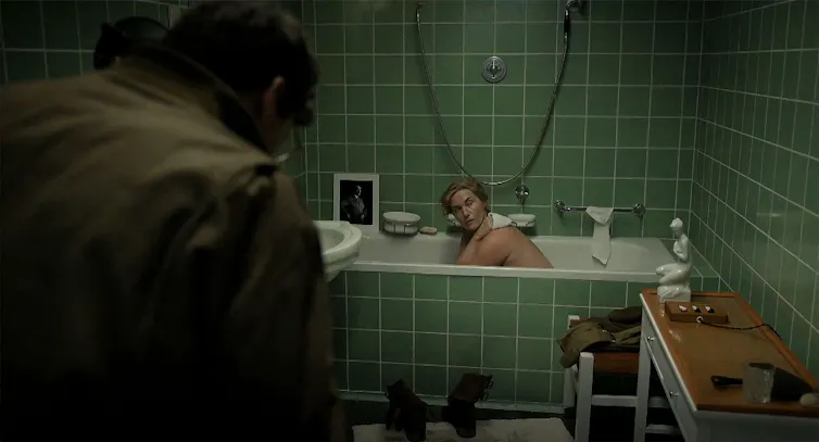 A woman sitting in a bath in a green-tiled bathroom
