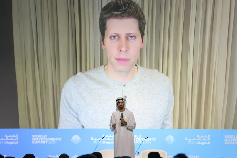 Photo of OpenAI CEO Sam Altman on a large screen behind a stage