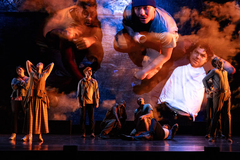 Production image: many people on a stage, and projected behind themselves.