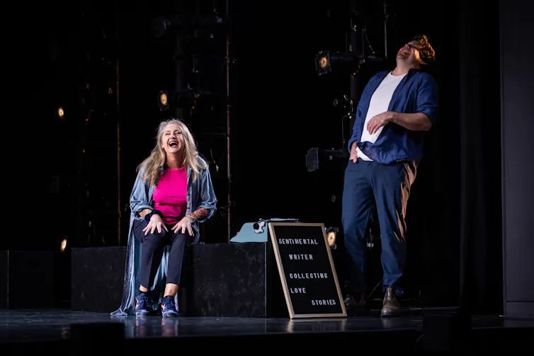 A man and a woman laugh on stage.