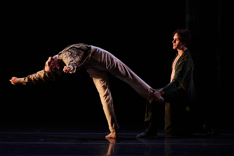Two men dance ballet on a stage.