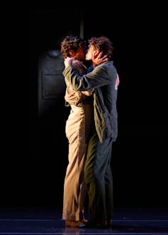 Two men kiss on a stage.