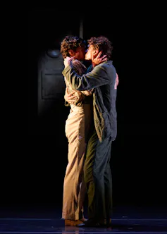 Two men kiss on a stage.