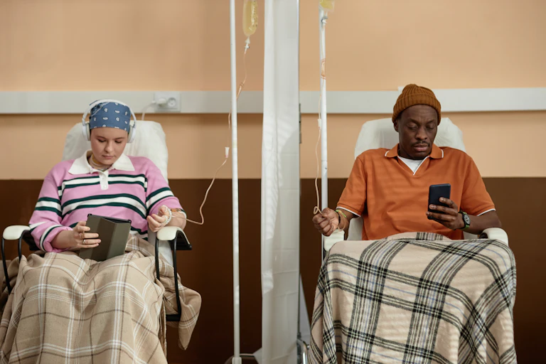 Front view at two people sitting in chairs with IV drip tubes and getting chemotherapy treatment in clinic