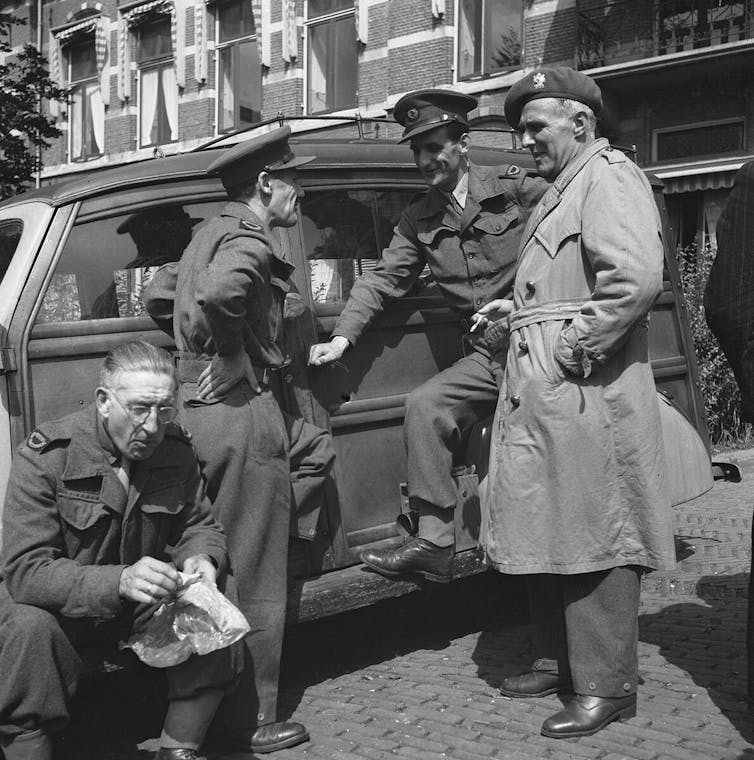 Black and white photo of soldiers talking by a car.
