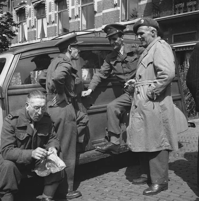 Black and white photo of soldiers talking by a car.