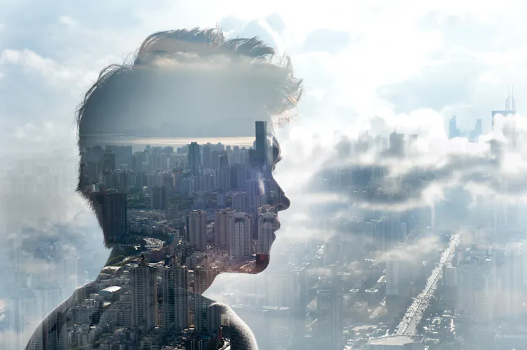 silhouette of someone looking out a skyscraper window at cityscape with clouds