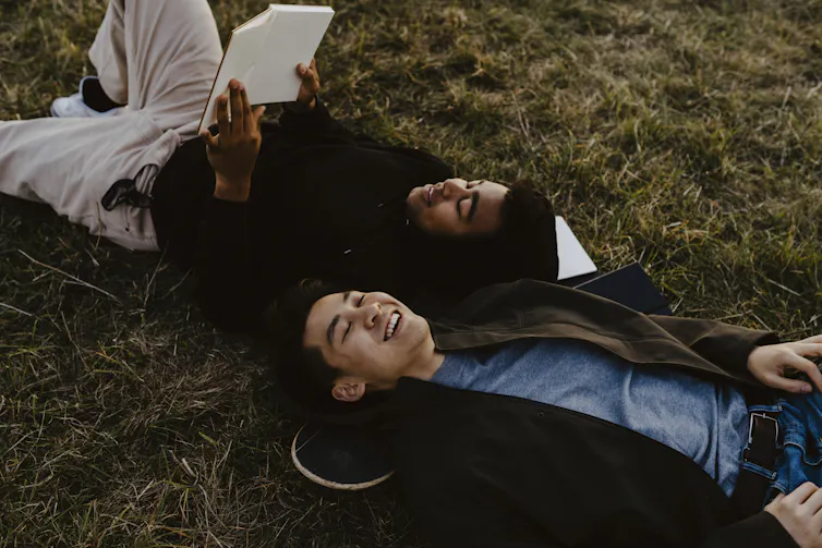 two young men lying on the grass looking at the sky