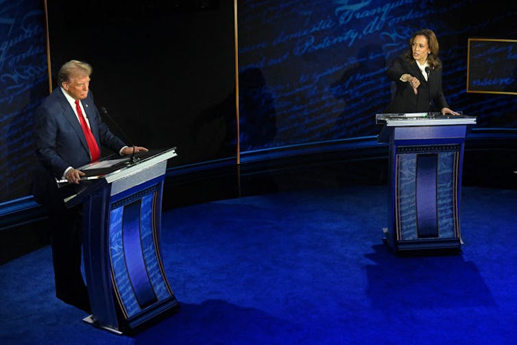 Harris and Trump behind their podiums on the debate stage, with Harris giving a thumbs down gesture