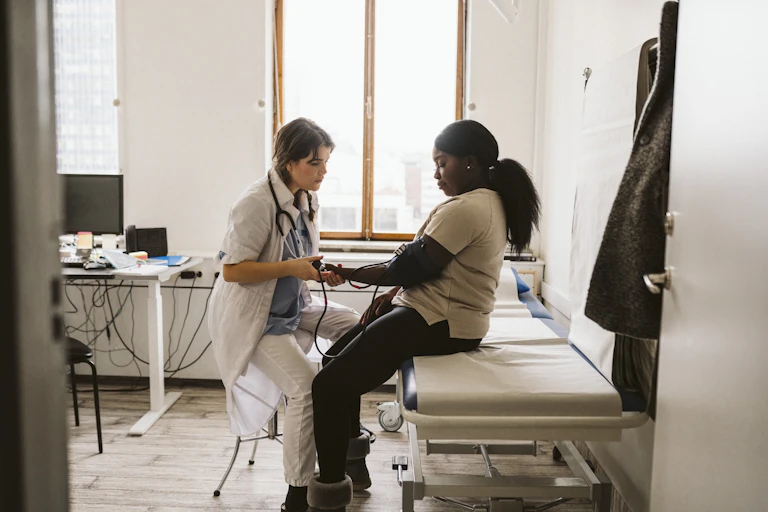 Clinician checking blood pressure of Black patient in exam room.