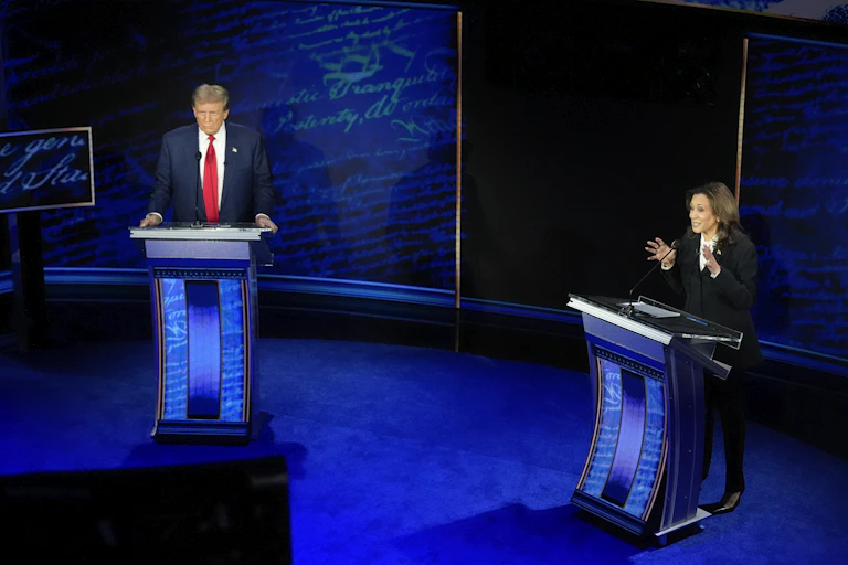 Two people stand at lecterns on a stage.