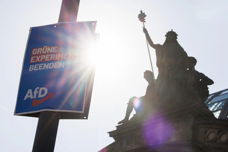 A lampost with an AfD election poster on it in front of a building featuring statues of gods.