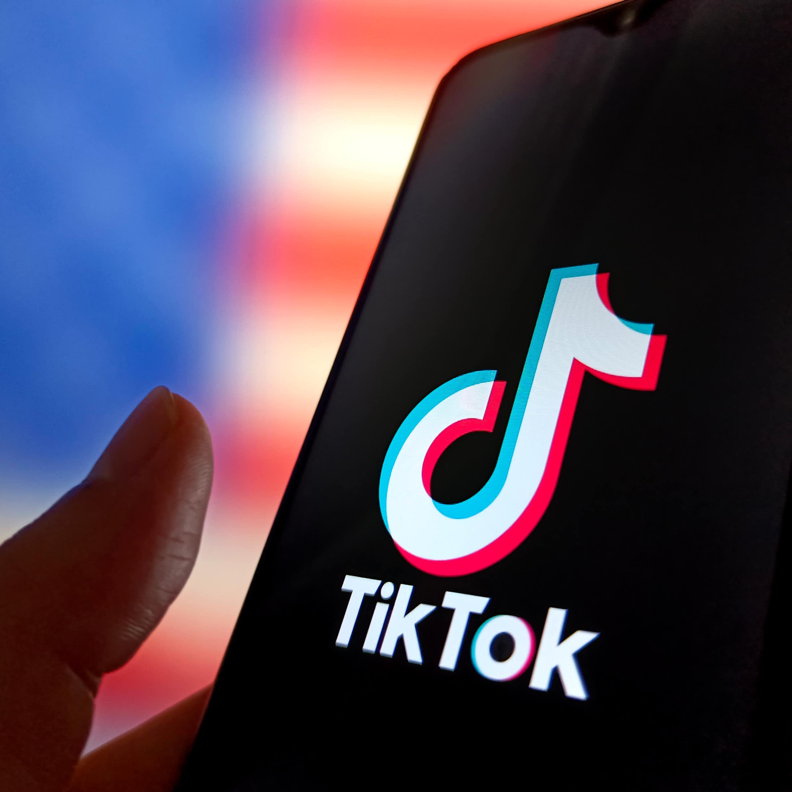 A hand holds a phone with the tiktok logo displayed.