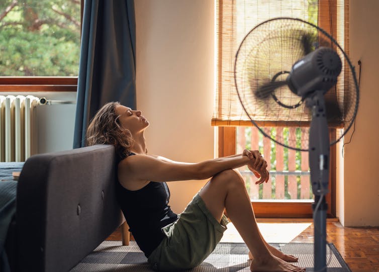 Young woman suffering from heat sitting at home on the floor in front of a fan
