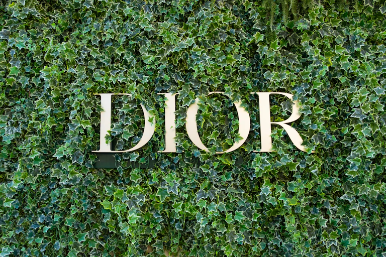 La marque DIOR en lettres dorées sur un fond de feuillage