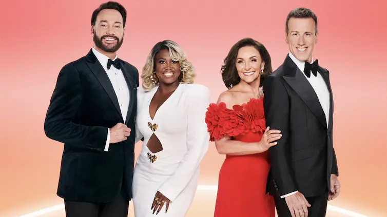 Two couples in evening dress, men in tuxedos and one woman in a white suit and one woman in a red dress.