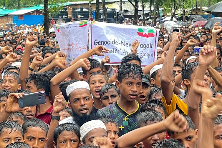 A group of men and woman stand with their fists aloft. A banner saying 'never again' is in the middle.
